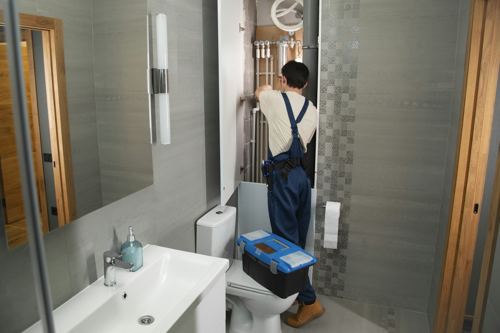 Plumber with a toolbox working on bathroom pipework