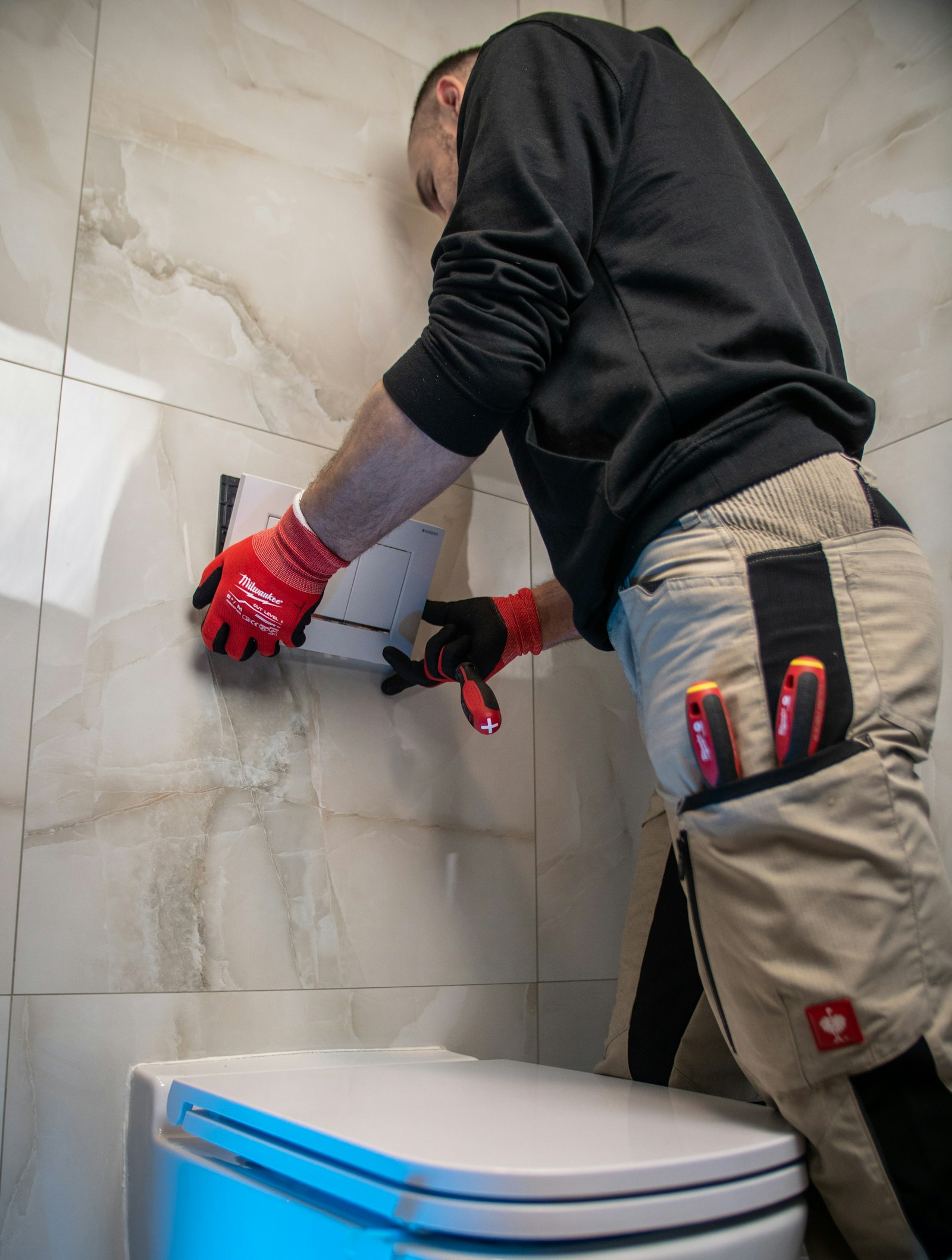 Plumber in work gloves fitting a wall-hung toilet