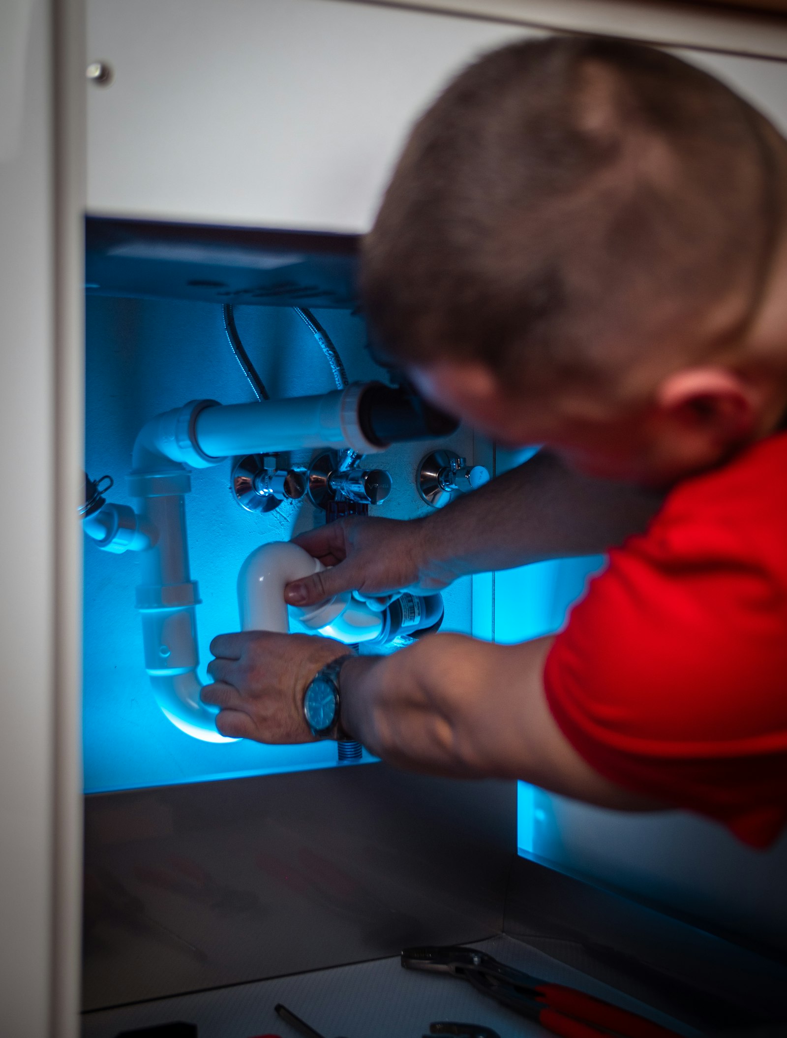 Plumber repairing pipework inside a sink cabinet